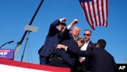 在宾夕法尼州竞选集会上受到枪击并受伤的前总统特朗普在美国特勤局特工保护和帮助下离开讲台。(2024年7月13日)