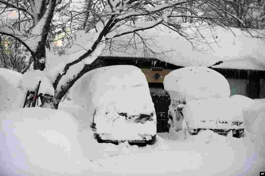 Cars with snow atop the roofs sit idle at a home on Broadway in Lancaster, N.Y., Nov. 19, 2014.