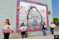 FILE - Activists hold signs promoting Native American participation in the US census in front of a mural of Crow Tribe historian and Presidential Medal of Freedom recipient Joe Medicine Crow on the Crow Indian Reservation in Lodge Grass, Mont., on Aug. 26, 2020.
