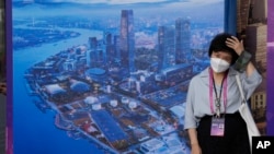 ແມ່ຍິງທີ່ໃສ່ໜ້າກາກອະນາໄມຄົນນຶ່ງ ຢືນຢູ່ໃກ້ພາບທີ່ສະແດງໃຫ້ເຫັນຜັງເມືອງໃນຊຽງໄຮ, ວັນທີ 6 ກໍລະກົດ 2023. ຈີນ ໄດ້ລາຍງານຜູ້ເສຍຊີວິດ 239 ຄົນ ຈາກພະຍາດ COVID-19 ໃນເດືອນມິຖຸນາ, ເຊິ່ງເປັນເດືອນທີ່ມີການເພີ້ມຂຶ້ນຢ່າງສໍາຄັນ ລຸນຫຼັງທີ່ພວກເຂົາເຈົ້າຍົກເລີກມາດຕະການການກັກໂຕ.