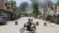 Young men riding a motorbike watch as smoke rises following an explosion allegedly set off by armed insurgents attempting to storm a military compound in Bannu, Pakistan, July 15, 2024. 