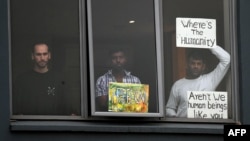 FILE - Three asylum seekers look out at protesters rallying outside in their support, from their hotel room where they have been detained in Melbourne, Australia, June 13, 2020.