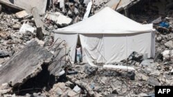 A displaced Palestinian stands at the entrance of a tent set up amid the rubble of a building damaged during Israeli bombardment in Rafah, on the southern Gaza Strip.