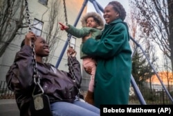 Derry Oliver, right, holds daughter Dessie, 2, while her other daughter, also named Derry, swings, Feb. 9, 2024, in New York. (AP Photo/Bebeto Matthews)