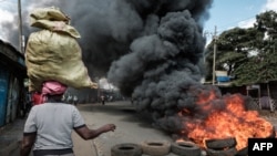 Picha hii inaonyesha mwanamke akibeba vitu vyake kichwani, akipita kando ya matairi yalichomwa katika mtaa wa Kibera, Nairobi, Machi 30, 2023 wakati wa maandamano ya upinzani. Picha ya AFP