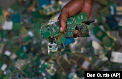 FILE - In this photo taken Monday, Aug. 18, 2014, a worker gathers handfuls of cellphone printed circuit boards from a pile to put in a sack for recycling, at the East African Compliant Recycling facility in Machakos, near Nairobi, in Kenya. (AP Photo/Ben Curtis, File)