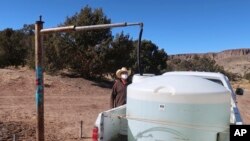 FILE - Phillip Yazzie waits for a water drum in the back of his pickup truck to be filled in Teesto, Arizona, on the Navajo Nation, Feb. 11, 2021. 
