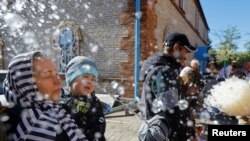 በሩሲያ ቁጥጥር ሥር ባለችው ማሪፑል በነበረው የፋሲካ አከባበር፣ አንድ ቄስ ምዕመናንን ጠበል ሲረጩ ያሳያል [ፎቶ ኤፒ ግንቦት 5፣ 2024.] 