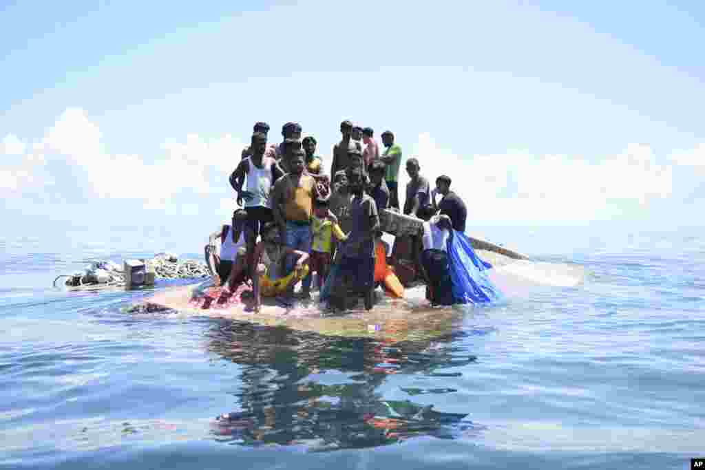 Rohingya refugees stand on their capsized boat before being rescued in the waters off West Aceh, Indonesia, March 21, 2024. 