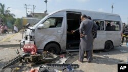 Pakistani investigators examine a damaged van at the site of a suicide attack in Karachi, Pakistan, April 19, 2024. 
