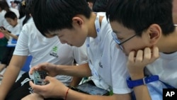 资料照片：2023年8月17日，在北京举行的年度世界机器人大会上，一名学生帮助他的同学通过智能手机玩网络游戏。（美联社照片）