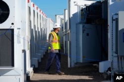 A worker checks battery storage at Orsted's Eleven Mile Solar Center on Feb. 29, 2024, in Coolidge, Ariz. Batteries allow renewables to replace fossil fuels while keeping a steady flow of power when sources like wind and solar are not producing. (AP Photo/Ross D. Franklin)