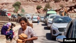 Msichana akipokea mikate kutoka kwa watu wanaojitolea huku wengine wakiwa wanangojea katika magari kifusi kiondolewe njiani kufuatia janga lililosababisha vifo la tetemeko la ardhi karibu na kijiji cha Tallat n'Yakoub, Morocco, Sept. 12, 2023