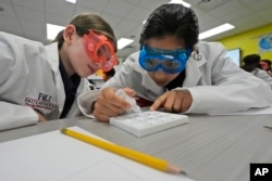 Twelve-year-olds Emma Starkman, left, and Jianna Landazabal-Echeverri test fake neurotoxins to determine which ailments afflicted their imaginary patients. (AP Photo/Wilfredo Lee)