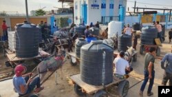 ফিলিস্তিনিরা গাজা উপত্যকার দেইর আল বালাহ আশ্রয়কেন্দ্রে একটি ওয়াটার ট্রিটমেন্ট স্টেশন থেকে পানীয় জল সংগ্রহের জন্য লাইনে দাঁড়িয়ে আছে। ( ২৭ অক্টোবর, ২০২৩)