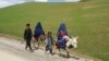 Afghan burqa-clad women ride donkeys alongside children on a road near Shah Mari village in Argo district, Badakhshan province, on May 1, 2024.
