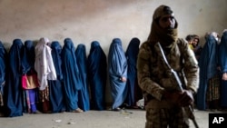 FILE - A Taliban fighter stands guard as women wait to receive food rations distributed by a humanitarian aid group, in Kabul, Afghanistan, May 23, 2023.