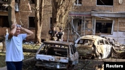 2024年8月11日，在俄罗斯库尔斯克地区，一名男子站在一栋多层住宅楼的院子里烧毁的汽车旁边。据地方当局称，这栋住宅楼被一枚被摧毁的乌克兰导弹的碎片击中。(路透社照片)