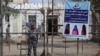 FILE - A Taliban prison security guard stands next to a poster ordering women to cover themselves with a hijab during the distribution of new uniforms ceremony by the Taliban authorities at a prison in Jalalabad, Feb. 5, 2023.