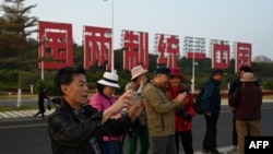 中国福建厦门竖立起一个台湾金门岛可以看到的“一国两制统一中国”的大型标语牌，游客在前拍照。（2024年1月12日）