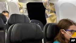 This image provided by Kelly Bartlett shows passengers near a hole in the fuselage of an Alaska Airlines Boeing 737 Max 9, Flight 1282, on Friday, Jan. 5, 2024. (Kelly Bartlett via AP)