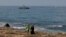 People walk along the beach as an Israeli navy vessel patrols the Mediterranean waters off Rosh Hanikra, known in Lebanon as Ras al-Naqura, on the Israeli side of the border between the two countries, on Oct. 7, 2022.