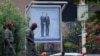 Pedestrians walk past a poster displaying Cameroonian President Paul Biya (R) next to his French counterpart Emmanuel Macron, in a street in Yaounde on July 25, 2022, prior to the French president's visit. 