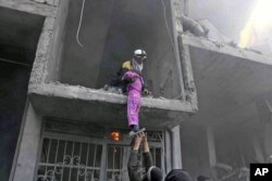 This photo released Feb. 21, 2018, provided by the Syrian Civil Defense group known as the White Helmets, shows a member of the Syrian Civil Defense group rescuing a young girl from a building damaged by airstrikes and shelling by Syrian government forces, in Ghouta, a suburb of Damascus, Syria.