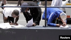 FILE - Abadabuka eZimbabweans balungisa amaphepha abo okusebenza lokuhlala kwele South Africa emawofisini awe-Immigration eJohannesburg. . (AP Photo/Denis Farrell)