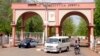 A man rides a motorbike taxi past police vehicles at the entrance of Shehu Shagari College of Education in Sokoto, Nigeria, May 13, 2022. Deborah Yakubu, who was killed May 12 over allegedly blasphemous statements, was a student at the school.