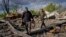 Villagers walk past unexploded artillery shells as they collect scrap metal from a bombed warehouse in the village of Malaya Rohan, Kharkiv region, May 18, 2022. 