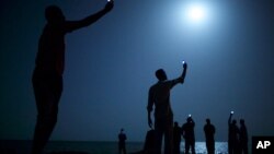In this photo provided on Feb. 14, 2014 by World Press Photo, the World Press Photo of the Year 2013 by John Stanmeyer, USA, VII for National Geographic, shows African migrants on the shore of Djibouti city at night, raising their phones in an attempt to capture an inexpensive signal from neighboring Somalia in Djibouti City, Djibouti.