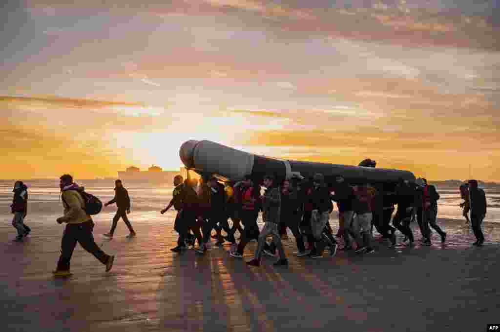 Migrants carry a smuggling boat on their shoulders as they prepare to embark on the beach of Gravelines, near Dunkirk, northern France, Oct. 12, 2022, in a attempt to cross the English Channel.