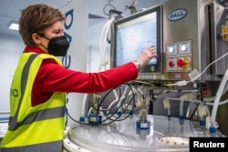 Menteri Pertama Skotlandia, Nicola Sturgeon mengoperasikan bioreaktor ekspansi sel saat meninjau pabrik vaksin Valneva Scotland yang baru di Livingston, Skotlandia, Inggris 28 Maret 2022. (Andy Buchanan/Pool via REUTERS)