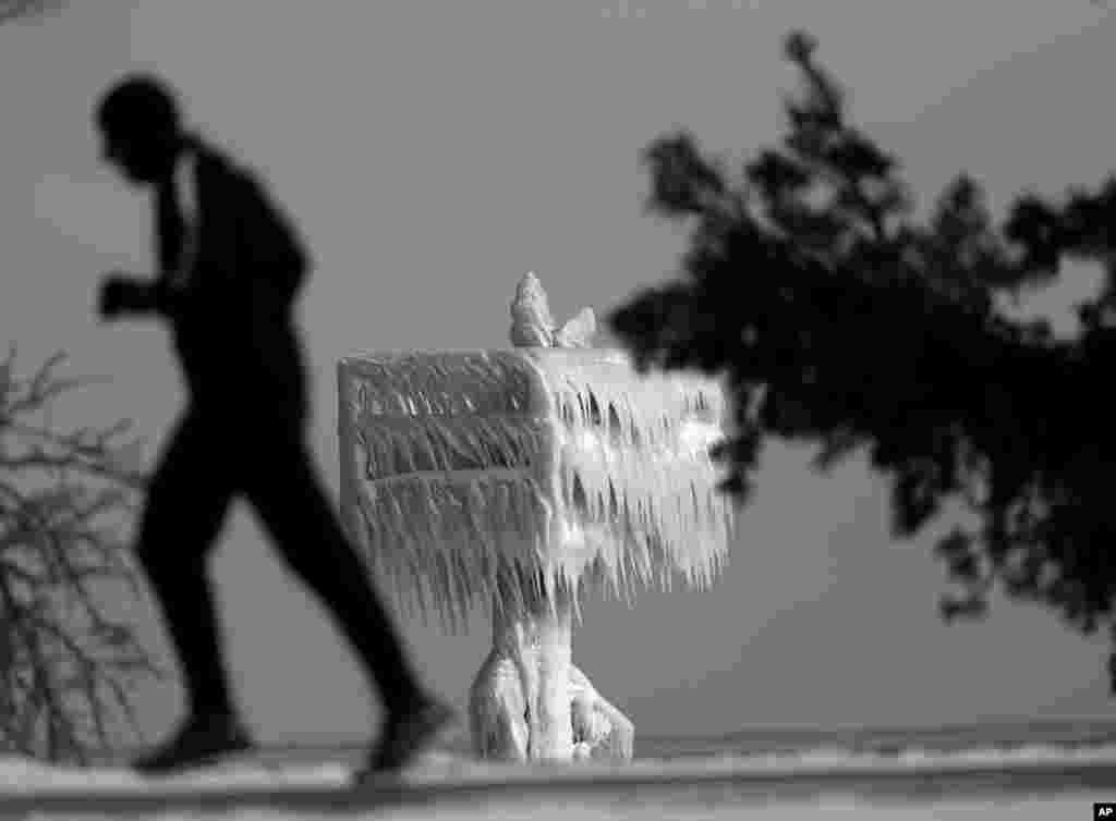 A lone runner jogs past a shore beacon encased by a combination of blowing snow and spray along Lake Michigan at the 31st Street beach in Chicago, Illinois, Jan. 16, 2018.