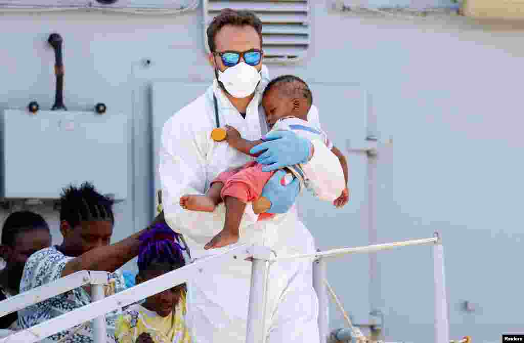 A doctor holds a baby as migrants disembark from Italian Navy ship Sirio in the Sicilian harbor of Augusta, Italy.