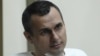 FILE - Oleg Sentsov sits behind glass in a cage at a court room in Rostov-on-Don, Russia, July 21, 2015. 