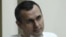 FILE - Oleg Sentsov sits behind glass in a cage at a court room in Rostov-on-Don, Russia, July 21, 2015. 