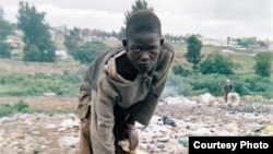 Street youth reaches for a battered football (soccer ball) with one hand while holding a glue bottle in the other. Credit Braitstein