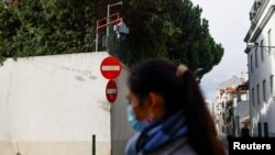 资料照片：一位女士从中国驻葡萄牙首都里斯本大使馆外走过，使馆墙头伸出一个监控摄像头，对着使馆外的街区。(2022年12月21日)