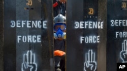 资料照片： 2021年3月11日，一名反政变抗议者从缅甸仰光设立的临时路障空隙中窥视。（美联社照片）