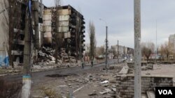 2022年4月6日，在基辅郊区城镇博罗江卡，少数居民骑着自行车经过被摧毁的楼群。(美国之音希瑟·默多克拍摄)