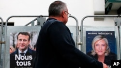 Yon moun pase devan kanpay afich kanpay prezidansyel pou Prezidan Emmanuel Macon, kandida santris la, ak kandida ekstrem dwat la Marine Le Pen nan vil Anglet, sidwes peyi La Frans, Vandredi 8 Avril, 2022. 