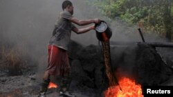 FILE - A man working at an illegal oil refinery site pours oil under a locally made burner to keep the fire going, near river Nun in Nigeria's oil state of Bayelsa.