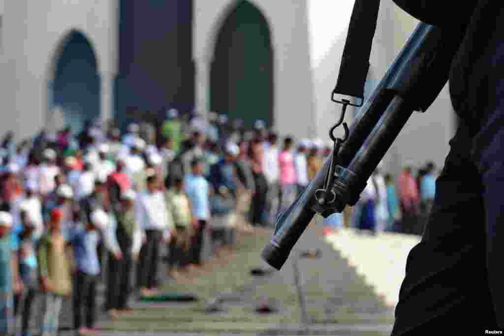 Orang-orang melakukan shalat Jumat sementara para anggota polisi berjaga-jaga di Dhaka, Bangladesh. Negara ini akan melakukan pemilihan umum pada hari Minggu. 