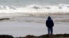 FILE - A man watches ocean waves crash at Seacliff State Beach in Aptos, California.