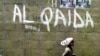 FILE - A girl walks past a wall with graffiti about the al-Qaida network in a Muslim area of the northern city of Kano, Nigeria.