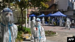 身穿防护服的工作人员在上海静安区的一个测试点看着居民做新冠病毒测试。（2022年4月4日）