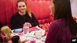 Marisa Dragos, 23, left, along with her childhood friend Lisa Costantino, 24, right, sit for lunch at American Girl Cafe with two store-borrowed dolls, Friday, Dec. 2, 2022, in New York. (AP Photo/Bebeto Matthews)