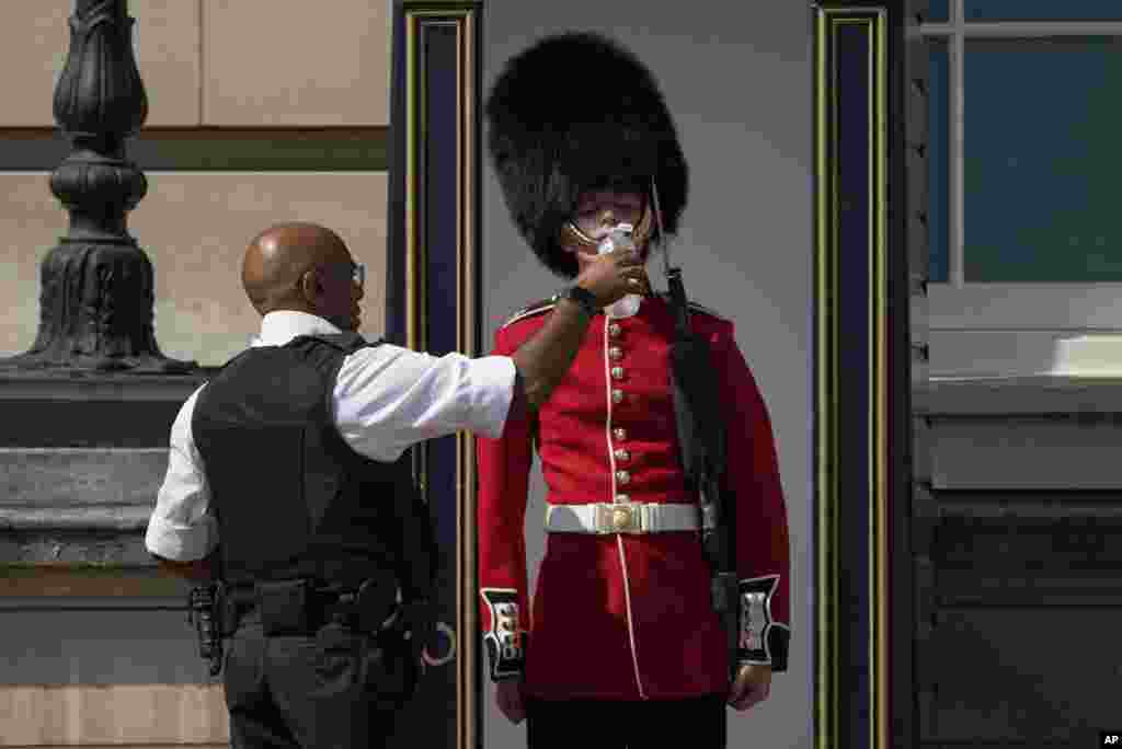 A police officer givers water to a British soldier wearing a traditional bearskin hat, on guard duty outside Buckingham Palace, during hot weather in London, July 18, 2022.&nbsp;The British government have issued their first-ever &quot;red&quot; warning for extreme heat when temperatures may reach 40&deg; C (104&deg; F) for the first time.
